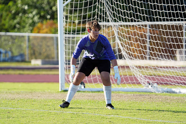Male goalkeeper diving mid-air to save goal during match on football pitch.