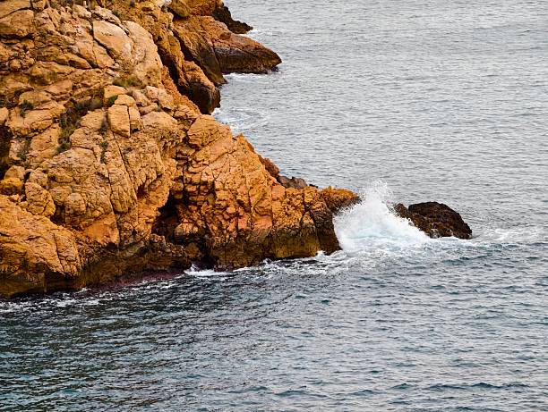 gentle surf breaking around warmtoned rocks, soft foam and subtle ripples, sunlit textures creating calm