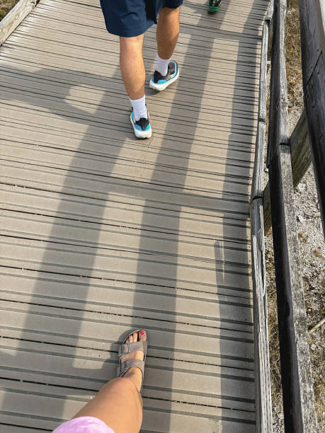 People walking on a wooden boardwalk, sunlight creating shadows