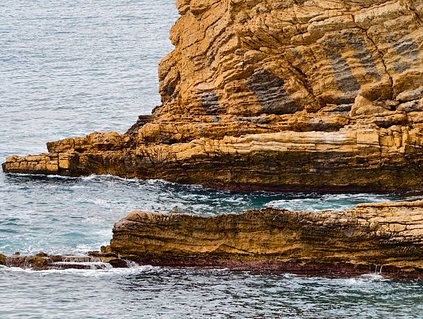 stratified cliff shelf meeting calm sea, vertical layers and weathered ledges, subtle tidal pools and gentle