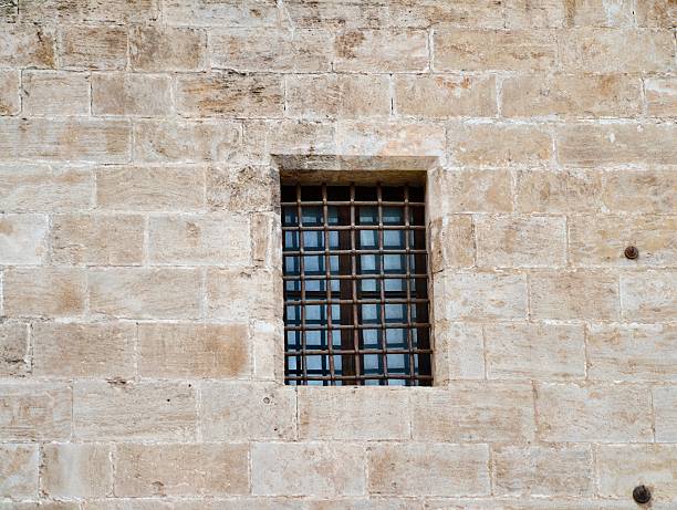 Small barred window set in stone wall, compact square opening with tight masonry joints