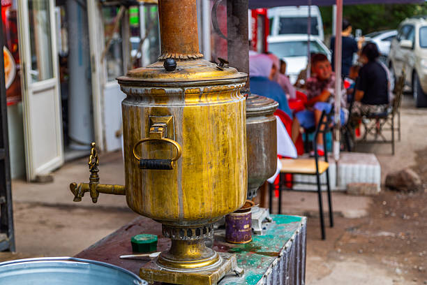 Multiple adults and children interact while enjoying tea from an antique samovar at a lively outdoor cafe. The scene is vibrant, showcasing social engagement and a casual atmosphere in Cholok, Kyrgyzstan - July 16, 2024