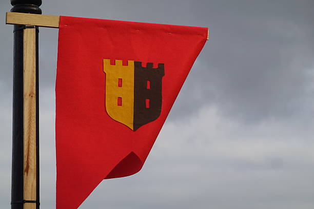Red flag with a golden and brown castle crest, representing a medieval heraldry symbol against a cloudy sky background