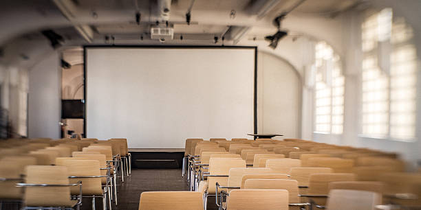 Modern conference room with beige chairs and a large projection screen. Natural light from tall windows creates a bright, inviting atmosphere. Ideal for business meetings, presentations, and collaborative brainstorming, emphasizing professionalism and focus.