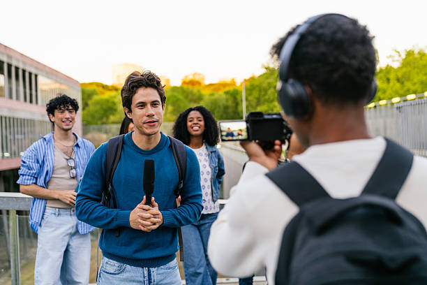 Student reporter holding a microphone, interviewing a diverse group of college students on university campus while cameraman films