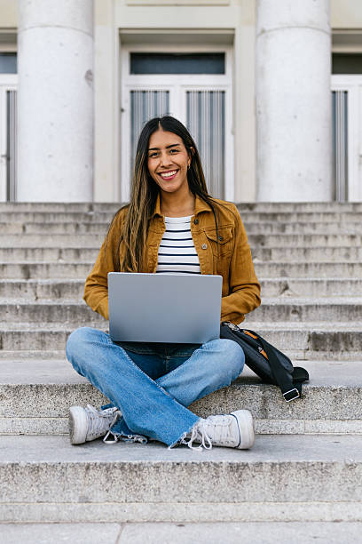 istock Young adult student smiling using laptop on campus steps 2256708479