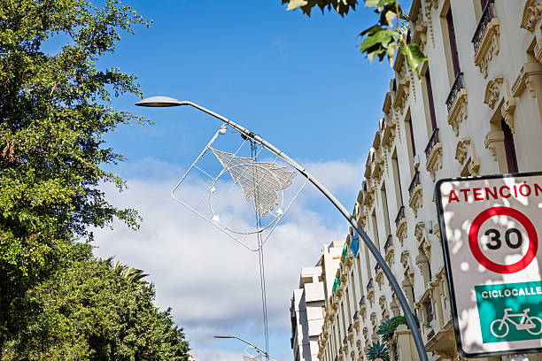 Santa Cruz, Tenerife, Spain, Europe - December 21th 2025: A Christmas decoration in the shape of a Christmas tree is seen hanging from a modern streetlight in Santa Cruz, the main city of Tenerife in the Canary Islands. The festive installation reflects the city’s seasonal street decorations, combining contemporary urban lighting with traditional holiday motifs in a subtropical setting.