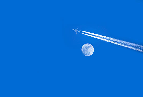 A large passenger plane, approaching Haneda Airport in a landing position, flies over the moon and high-rise office buildings as it heads towards the central part of Tokyo.