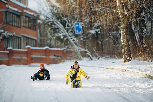 Happy mother and son playing in the snow, smiling while sliding down a winter park slope enjoying outdoor fun