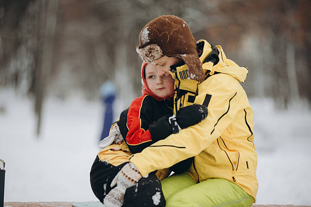 Mother and young son embrace in snowy park, bundled in winter gear, sharing warmth and joyful family bonding outdoors