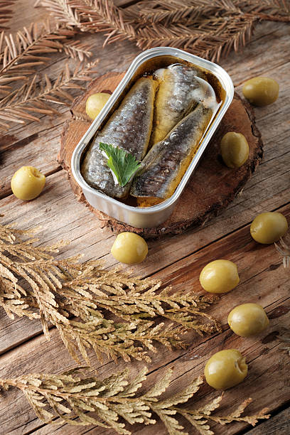 Sardines in Oil Placed on Wooden Surface With Olives and Leaves Around