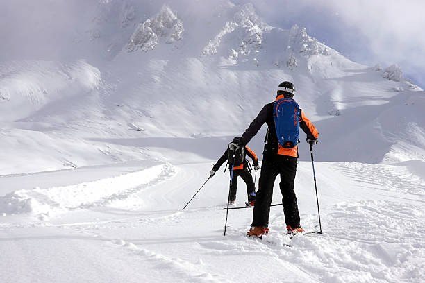 Dynamic action shot of a young female skier navigating powder snow, photographed from below against brilliant blue sky. Snow particles create dramatic effect around athletic figure.