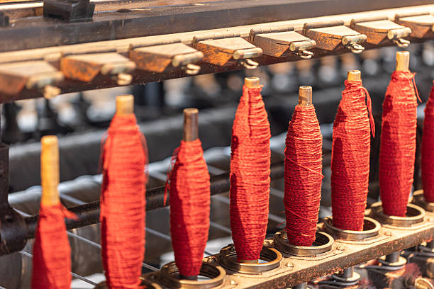 Red yarn spools lining an old textile spinning machine, showing industrial heritage, manufacturing tradition, and the process of thread production in a factory setting