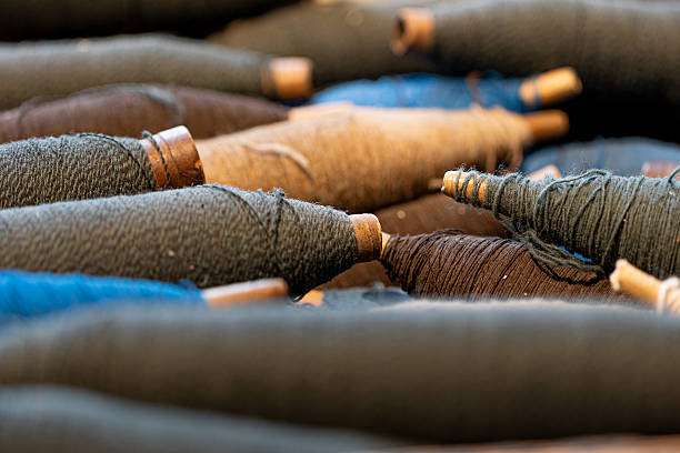 Spools of dark blue, brown, beige, and black woolen yarn are ready for weaving, representing traditional craftsmanship, textile production, and the intricate process of fabric creation