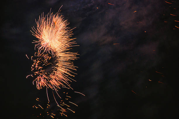 The night is illuminated by multicolored, vibrant fireworks, sparkling orange with green accents. Perfect for backgrounds and textures, event marketing, and festive images that convey energy and emotion.