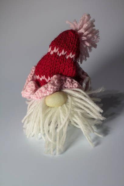 A small, handcrafted Scandinavian Christmas gnome (tomte) with a red knitted hat and white yarn beard, placed on a neutral background.