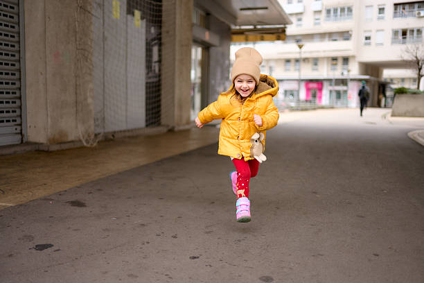 Sweet little girl runs outside the building on a cold day.