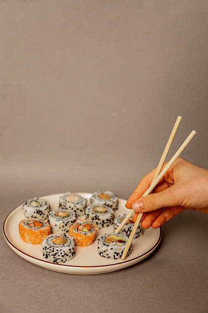 hand using chopsticks to take sushi from plate copy space isolated