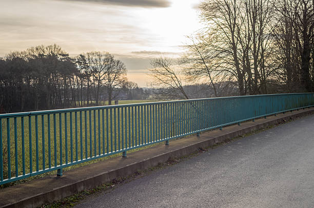 Bridge railing along asphalt road with trees and fields in heiden, germany