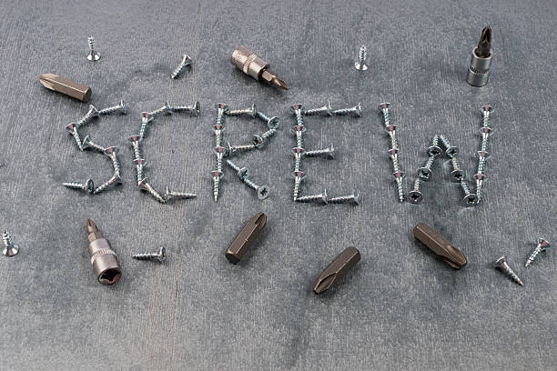 Unique screw arrangement forming the word 'SCREW' with scattered tools on a gray textured background, ideal for DIY, construction, or industrial concepts