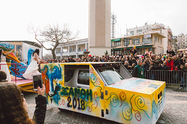 Xanthi, Greece - February 18, 2018: Colorful carnival float featuring a large peacock sculpture and female performers in white costumes moves through the central square of Xanthi during the annual Xanthi Carnival, as crowds gather to watch, photograph, and celebrate one of the most important cultural festivals in northern Greece