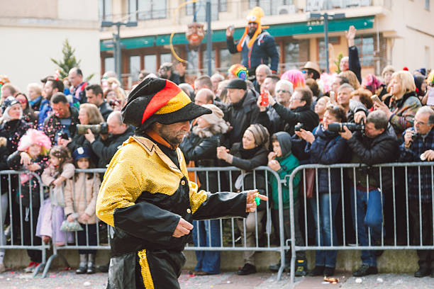 Man with painted face in a red coat with colorful scarf and a red cap with classic swimming goggles during the Rosenmontag carnival parade in Cologne