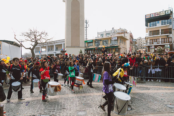 Xanthi, Greece - February 18, 2018: A large drum band performs energetic rhythms in front of a crowd during the annual Xanthi Carnival, with musicians wearing colorful outfits and themed shirts as they march along the parade route near the main stage, entertaining spectators and creating a vibrant atmosphere filled with music, movement, and celebration in the city center