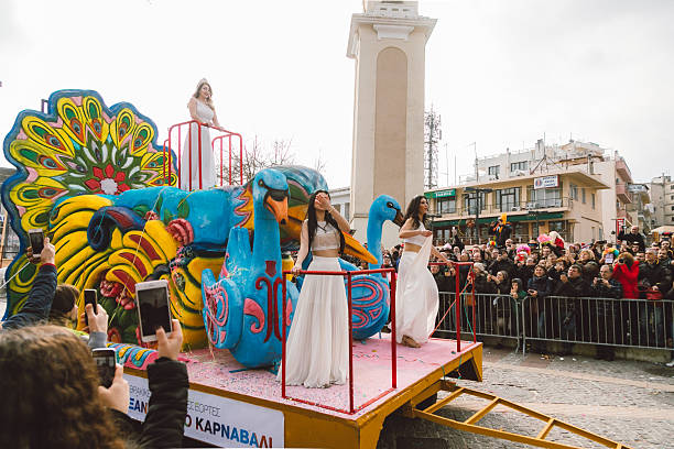 Xanthi, Greece - February 18, 2018: Colorful carnival float featuring a large peacock sculpture and female performers in white costumes moves through the central square of Xanthi during the annual Xanthi Carnival, as crowds gather to watch, photograph, and celebrate one of the most important cultural festivals in northern Greece