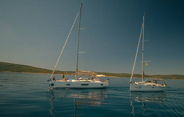 Two Yachts Anchored On Calm Sea, Twilight Casting Golden Reflections On Glassy Water, Distant Coastline