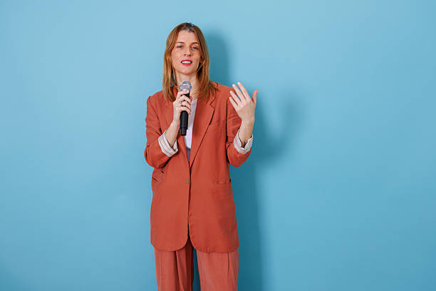 istock Woman public speaking holding microphone against blue background, presenting ideas and communicating message 2256744947