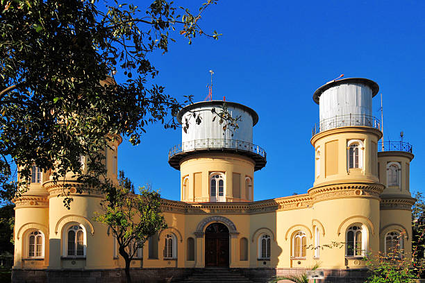 A large white telescope is on a hill with a clear blue sky. The telescope is the main focus of the image, and the hill and sky provide a serene and peaceful backdrop