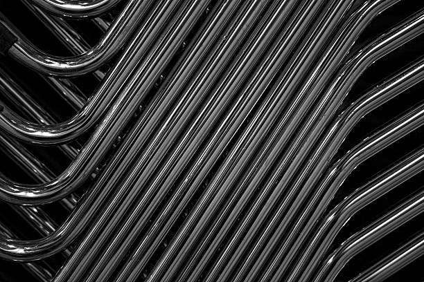 High-contrast black and white abstract photograph of curved metal tubes forming a repeating industrial pattern. A modern, minimalist image highlighting geometry, texture, and metallic reflections, ideal for contemporary design, backgrounds, and editorial or commercial use.