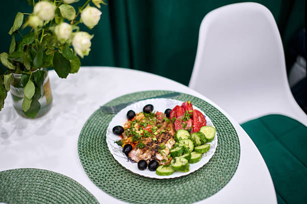 Plate with colorful salad and olives on white table, green decor accents. Bright light emphasizes fresh ingredients, creating lively dining atmosphere