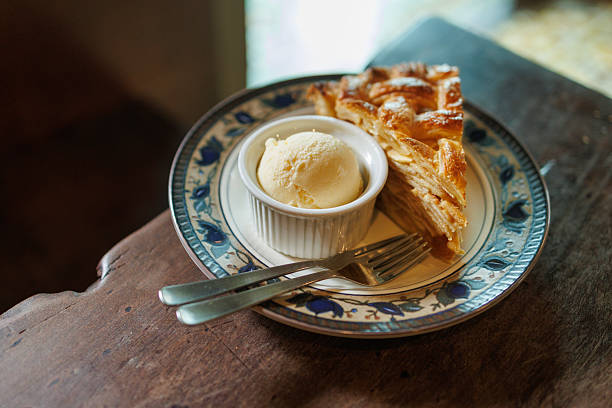 A slice of homemade apple pie served with a scoop of vanilla ice cream on a decorative plate, photographed from above on a rustic wooden table.