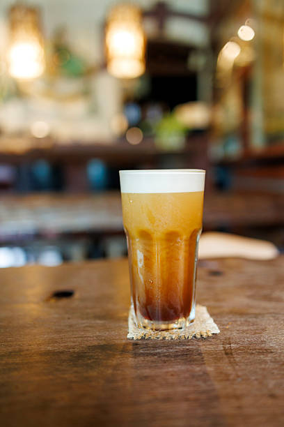 Iced shaken robusta coffee served in a tall glass with a light foam layer on top, placed on a wooden table in a cozy cafe environment.