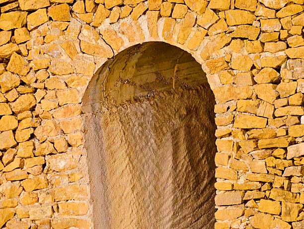 Sunlit sandstone arch doorway framing deep shadowed interior and curved recessed passage, textured stone