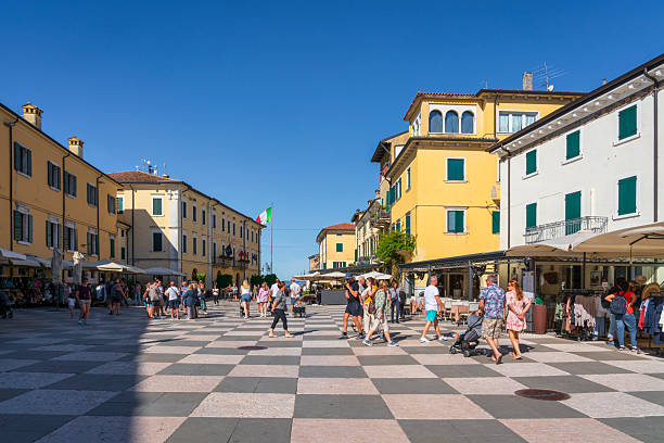 LAZISE, VENETO - ITALY - SEPTEMBER 6, 2025 People walking in Piazza Vittorio Emanuele in Lazise. Historic town center with checkered pavement on Lake Garda, Veneto, Italy.