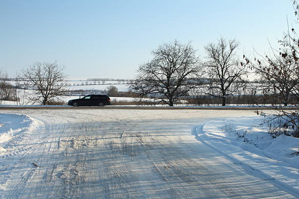 A car driving on a road in the snow. Snow. Sky. Outdoor. Tree. Covered