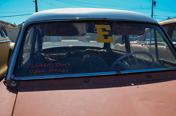 A detailed shot of a rusted mid-century automobile in a desert junkyard. The dusty windshield features a prominent yellow \