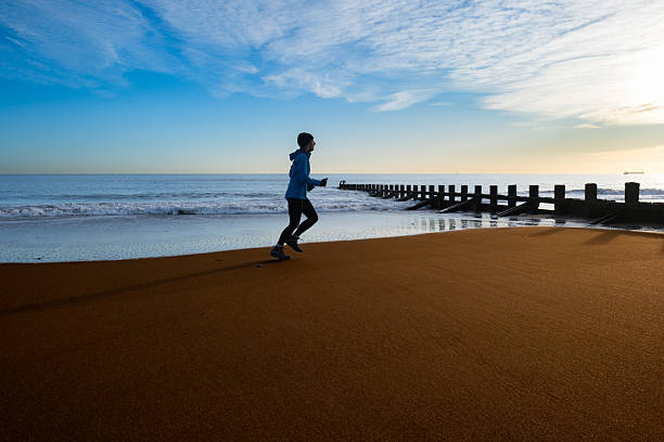 Senior woman running on the beach just north of Aberdeen, Scotland, as dawn breaks. With the tide going out, the sand is free of footprints.