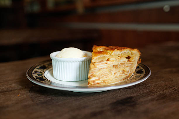 A slice of homemade apple pie served with a scoop of vanilla ice cream on a decorative plate, photographed from above on a rustic wooden table.