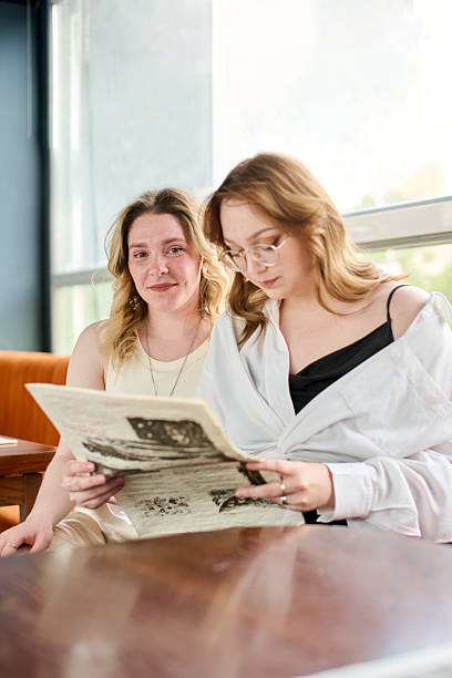 istock Young women reading newspaper together in bright cafe 2256755363