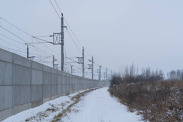 cold winter day with snow and ice in rural landscape, wall dividing railroad track from snow covered path