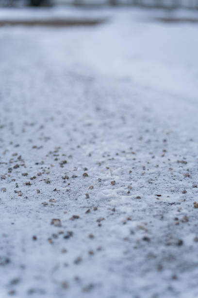 detail of snowy pavement with grit in village on cold day in winter, shallow focus in the middle, foreground and background blurred