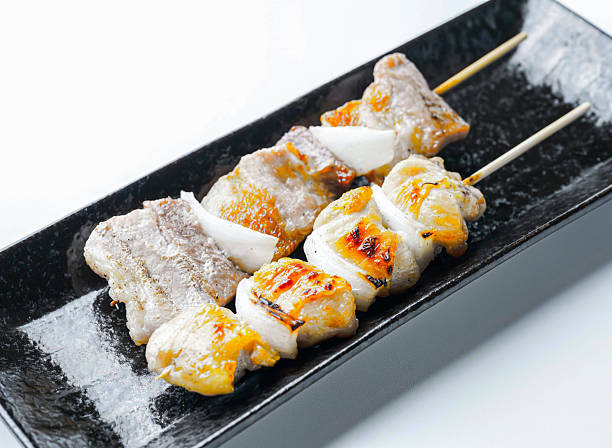 Grilled pork skewers with onions on black plate closeup view isolated on white background