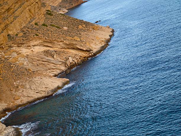 curving stratified coastline meeting gentle waves, layered cliffs and textured rock shelves creating rhythmic