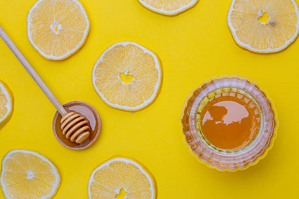Bright yellow background with honey and lemon slices arranged around a jar and honey dipper creating a cheerful scene