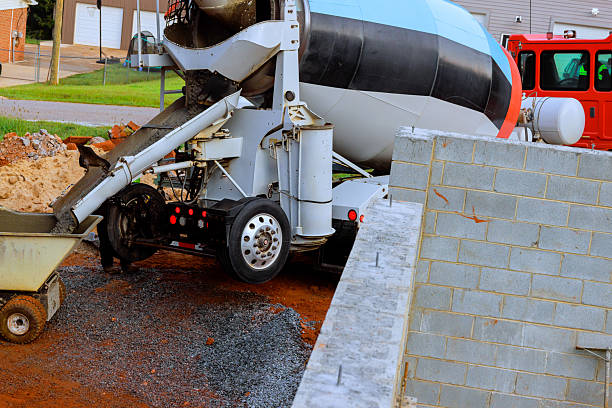 Workers use cement mixer to pour concrete at construction site near new walls in residential area.