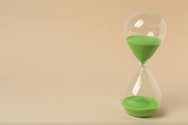 Hourglass with flowing sand on beige background. Space for text