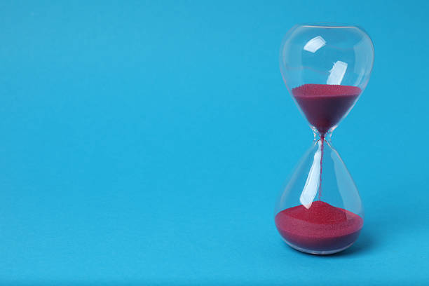 Hourglass with flowing sand on a blue background. Space for text